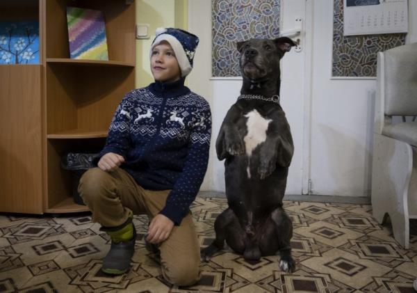 A boy poses for with an American Pit Bull Terrier in the Center for Social and Psychological Rehabilitation in Boyarka Ukraine, on Dec. 7, 2022.
